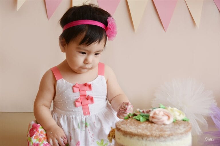Cute baby making a mess and looking at cake during a cake smash session in Surrey studio