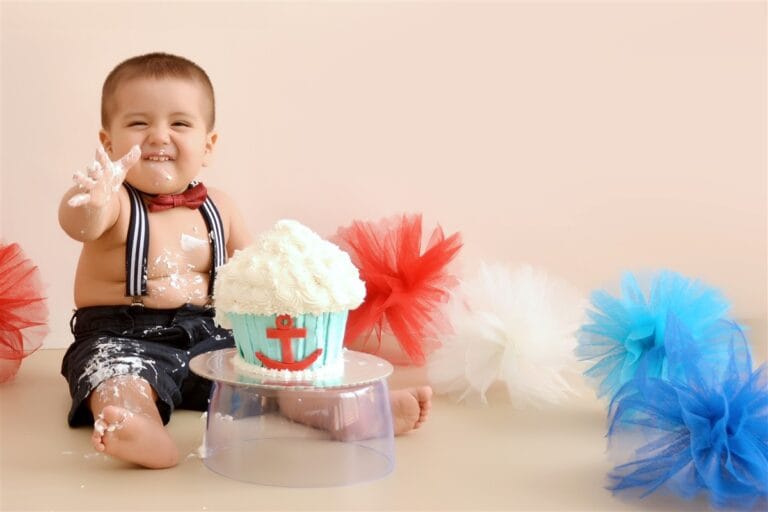 Adorable baby with giant cupcake in front enjoying a fun cake smash photography session in New Malden.