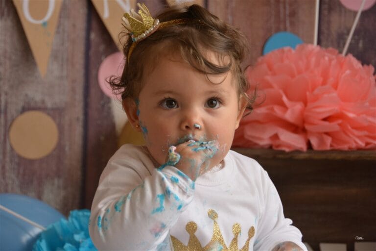 Happy baby eating cake during a first birthday cake smash in a Kingston Upon Thames photography studio
