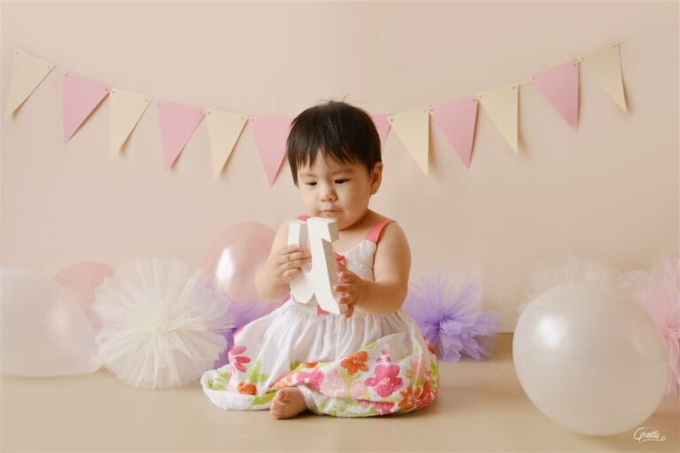 Beige and pink cake smash session with a one-year-old baby holding letter N in Kingston upon Thames.